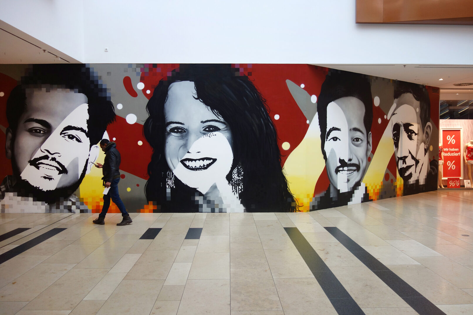 Köln Arcaden — Portrait-Wände mit Passant und Retail-Kontext